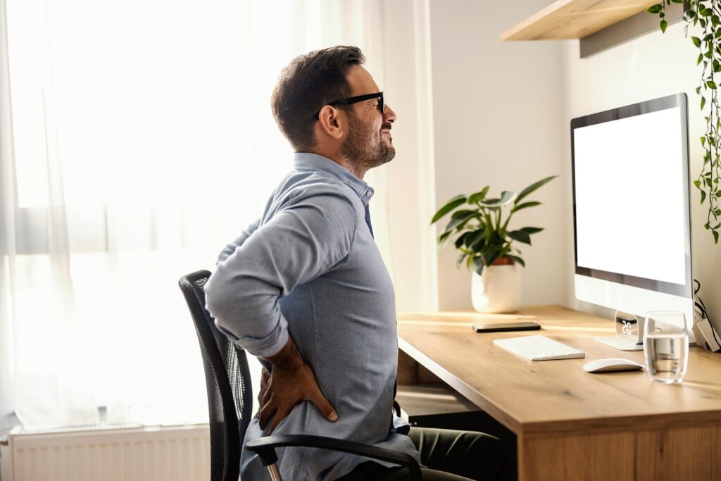 A Man working on desktop and holding his back due to back pain | Hudson Premier PT & Sports in Union City, Jersey City, NJ