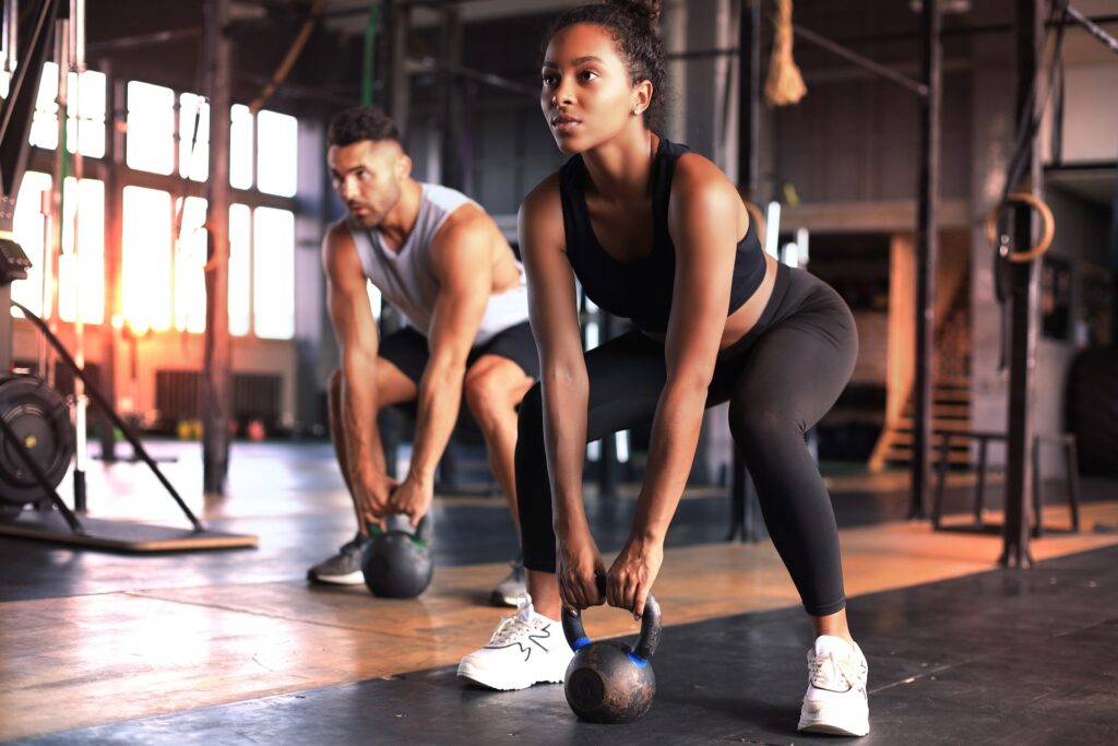 Fit and muscular couple focused on lifting a dumbbell during an exercise class in a gym | Hudson Premier PT & Sports | Jersey City | Union City | NJ
