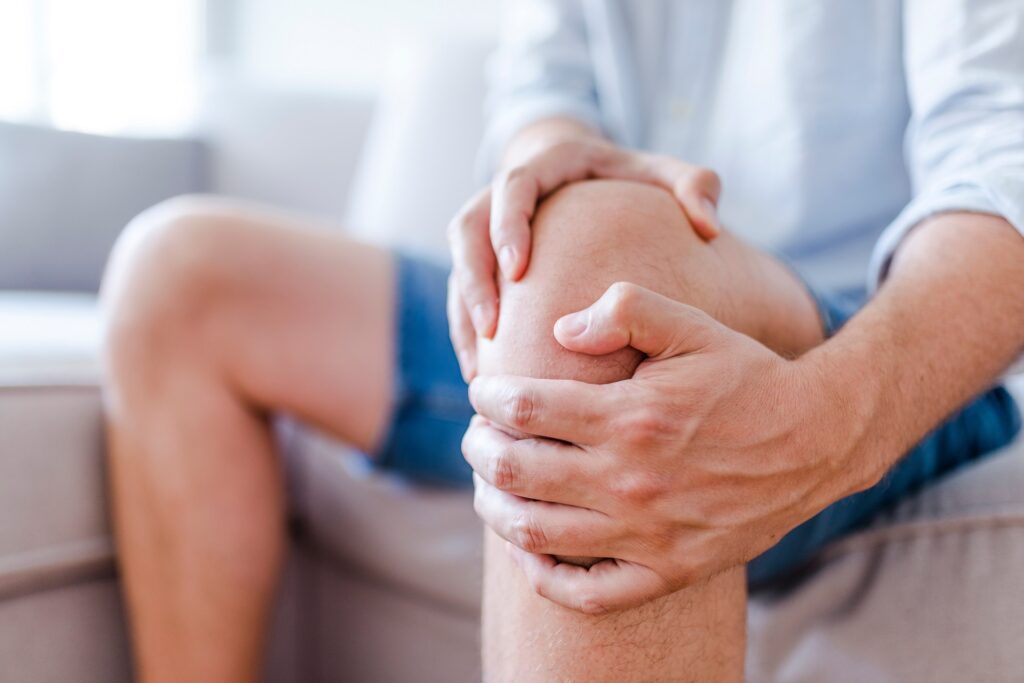 Man suffering from knee pain sitting on sofa | Hudson Premier PT & Sports in Union City, Jersey City, NJ