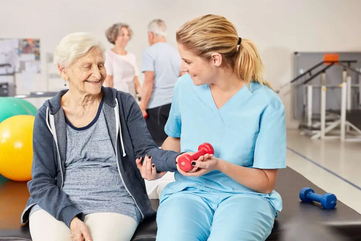 Elderly woman doing occupational therapy exercises with therapist using hand weights