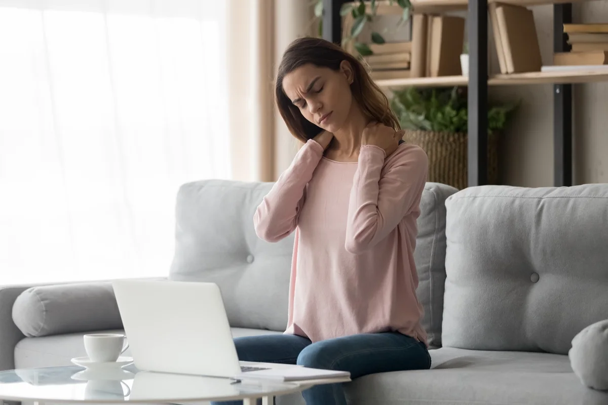 Woman experiencing Muscle Pain and neck discomfort while sitting on a sofa